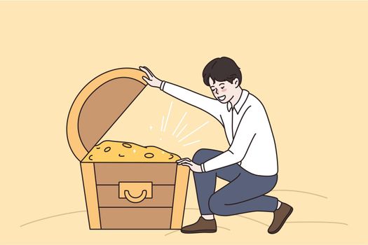 Success wealth and riches concept. Young smiling man sitting and looking at chest full of golden coins hidden treasures money vector illustration