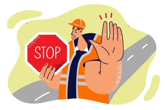 Man in builder uniform shows stop sign and makes caution gesture to warn drivers about road repairs. Repairman demonstrates inscription stop forbidding passage due to construction work