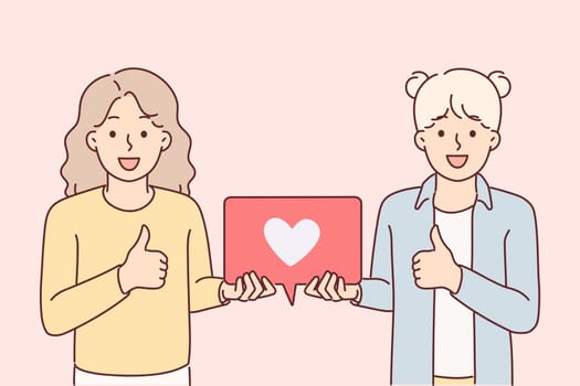 Teenage girls showing thumbs up and holding like icon for social media feedback concept. Little bloggers offer to put like under post or publication on site, demonstrating poster with heart