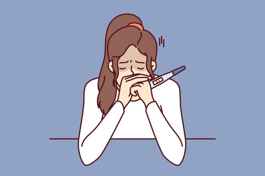 Frustrated pregnancy woman is crying holding pregnancy test with two strips and sitting at table. Concept pregnancy and need for family planning or problems associated with rejection of contraception