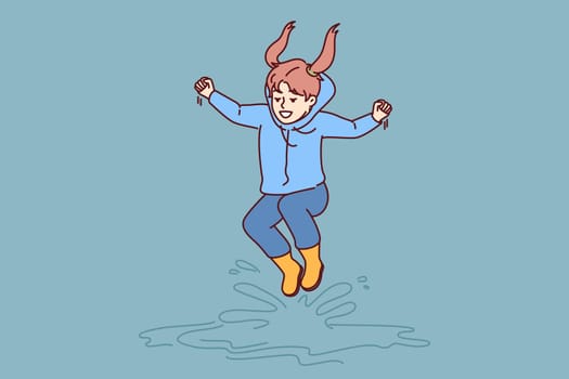 Little girl jumps in puddles in rubber boots and enjoys rainy autumn weather. Laughing child dressed in raincoat plays and bounces in puddles and has fun rejoicing in walk in fresh air