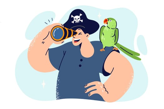 Little boy in pirate hat looks through spyglass and holds parrot on shoulder, dreaming of going on sea voyage. Schoolboy wants to be pirate or sailor and sail ocean on ship, leading team of sailors
