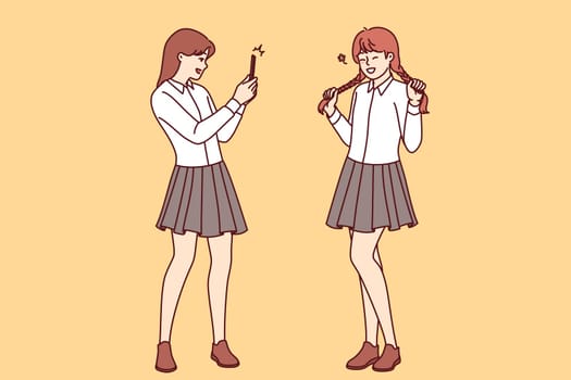 Teenage girls had photo shoot in school uniforms, posing for avatar for mobile application on social network. Female student takes photo friend on smartphone to post portrait on personal internet blog