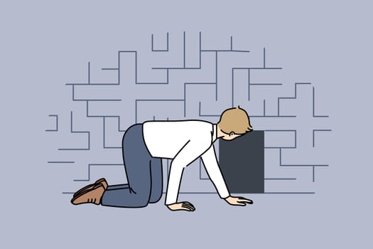 Man searching exit from labyrinth, crawling on floor near miniature door, as metaphor for difficult life situation. Guy is looking for way out of labyrinth, and needs hint or help.